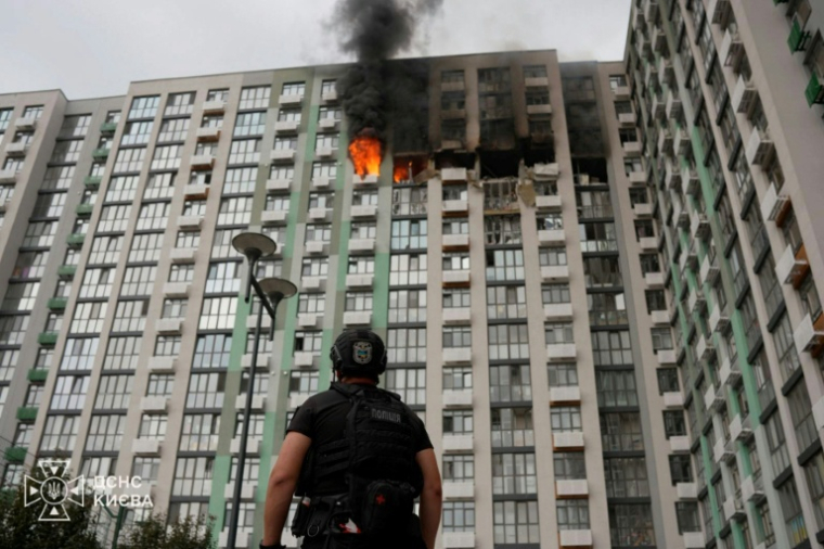 Photo prise et publiée par les services de secours ukrainiens le 1er septembre 2026, montrant un policier devant un immeuble d'habitation en feu à Kiev, après une frappe russe ( Service de secours ukrainiens / Handout )