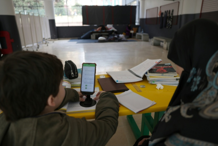 Une femme, assise à côté d'un enfant, supervise ses études en ligne sur un téléphone portable dans une école publique transformée en refuge pour personnes déplacées, à Dekwaneh, au nord de Beyrouth, le 25 mars 2026 au Liban ( AFP / Anwar AMRO )