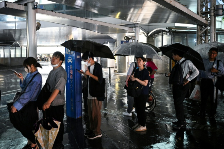 Des personnes attendent un taxi à la station de métro de Chiba, dans la ville de Chiba à l'est de Tokyo, le 13 août 2026, alors que de fortes pluies s'abattaient sur la région ( AFP / Philip FONG )