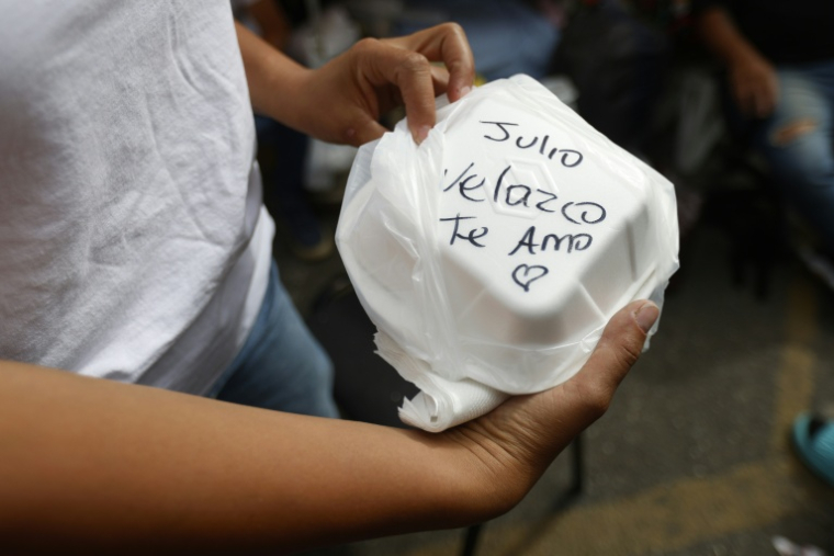 Maria Escalona tient un récipient jetable de nourriture sur lequel est écrit "Julio Velazco, je t’aime" pour son mari, un prisonnier politique, le jour de son anniversaire devant la prison de la Zone 7 de la Police nationale bolivarienne (PNB) à Caracas, le 20 février 2026 ( AFP / Pedro MATTEY )
