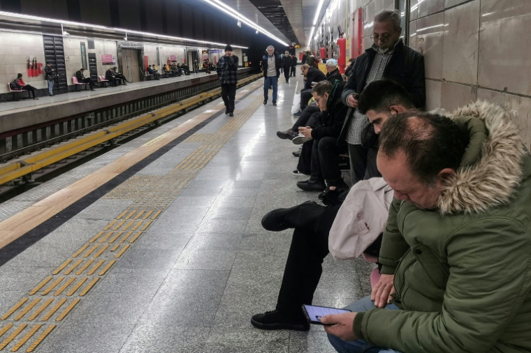 Des Iraniens regardent leurs téléphones portables en attendant le métro, à Téhéran le 24 janvier 2026 ( AFP / ATTA KENARE )