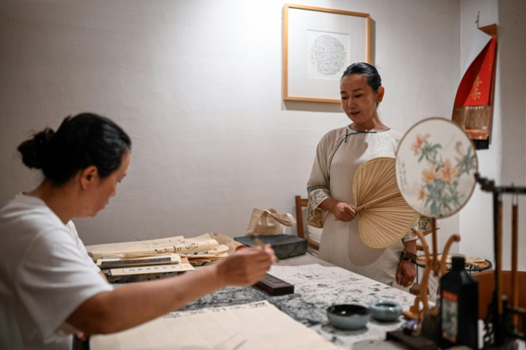 Yang Yun (d), fondatrice de l'espace de cohabitation pour femmes "Her Space", regarde une invitée faire de la calligraphie à Hangzhou, le 14 juillet 2025 dans la province du Zhejiang, dans l'est de la Chine ( AFP / Jade GAO )