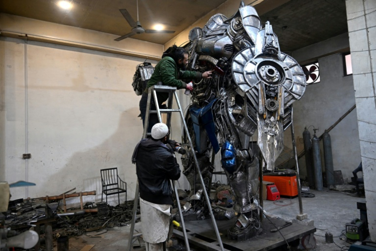 Le sculpteur Ehtisham Jadoon (en haut) peint à la bombe un Optimus Prime, personnage du film Transformers, fabriqué à partir de ferraille dans son atelier situé à la périphérie d'Islamabad, le 30 janvier 2026 au Pakistan ( AFP / Farooq NAEEM )