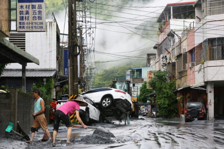 Des habitants nettoient la boue devant chez eux, avec des véhicules renversés en arrière-plan, après la rupture d'une digue au passage du super typhon Ragasa, à Hualien à Taïwan, le 24 septembre 2025 ( AFP / Johnson LIU )
