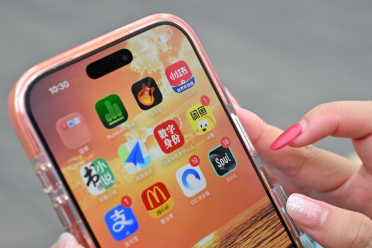 Une utilisatrice de Xiaohongshu se prépare à ouvrir l'application chinoise (en haut à droite) alors qu'elle visite la Cité interdite à Pékin, le 11 juillet 2026 ( AFP / ADEK BERRY )