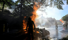 Manifestant devant une poubelle en feu lors d'une manifestation anti-G7 à Genève, le 14 juin 2026 ( AFP / Gabriel Monnet )