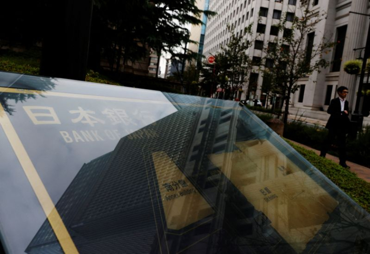 Photo d'un homme qui passe devant une pancarte de la Banque du Japon devant son siège à Tokyo