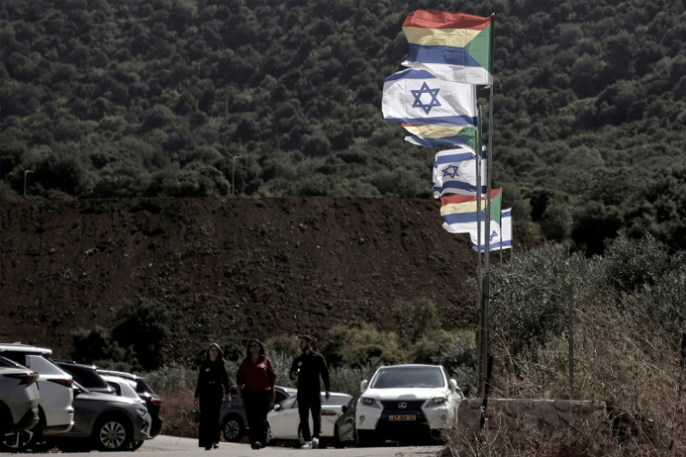 Des habitants passent près de drapeaux israéliens et druzes dans le village druze d’Ein Qiniyye, sur le plateau du Golan annexé par Israël, le 4 octobre 20260 Druze residents have long rejected any sign of allegiance to Israel, as accepting Israeli citizenship or casting a vote could lead to ostracism. The landscape today, however, is changing: according to Israel's interior ministry, 45 percent of them now hold Israeli citizenship, compared to just 2 percent forty years earlier. ( AFP / Jalaa MAREY )