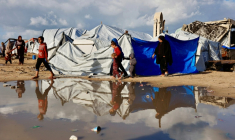 Des Palestiniens marchent près d'une flaque d'eau après des inondations dans un camp de déplacés, le 28 décembre 2025 dans la ville de Gaza ( AFP / Omar AL-QATTAA )