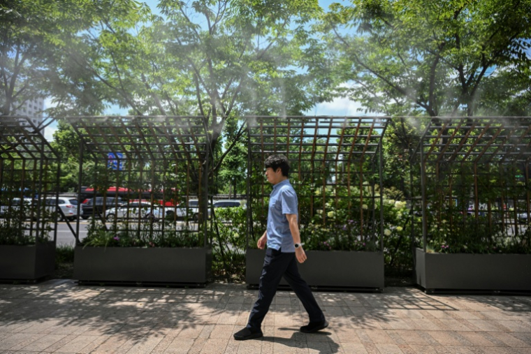 Un homme passe devant une rampe de brumisateurs installés dans une rue de Séoul, le 12 juillet 2026  ( AFP / JADE GAO )