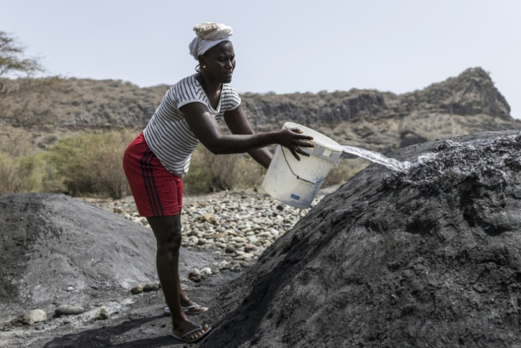 Vania Tavares verse de l'eau sur un tas de sable noir, sur une plage dégradée par l'exploitation commerciale, près de Ribeira da Barca, le 20 mai 2026 au Cap-Vert ( AFP / PATRICK MEINHARDT )