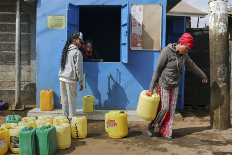 Margaret John (d) récupère des jerrycans d'eau propre à un point de distribution après avoir échangé des points gagnés en livrant des déchets plastiques à un point de collecte de l'ONG Human Needs Project (HNP) dans le bidonville de Kibera, à Nairobi, le 11 août 2025 au Kenya ( AFP / Tony KARUMBA )