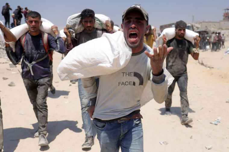 Des Palestiniens transportent des sacs de farine après que des camions d'aide sont entrés dans la bande de Gaza assiégée par Israël depuis le poste frontière nord de Zikim, le 27 juillet 2025 ( AFP / BASHAR TALEB )