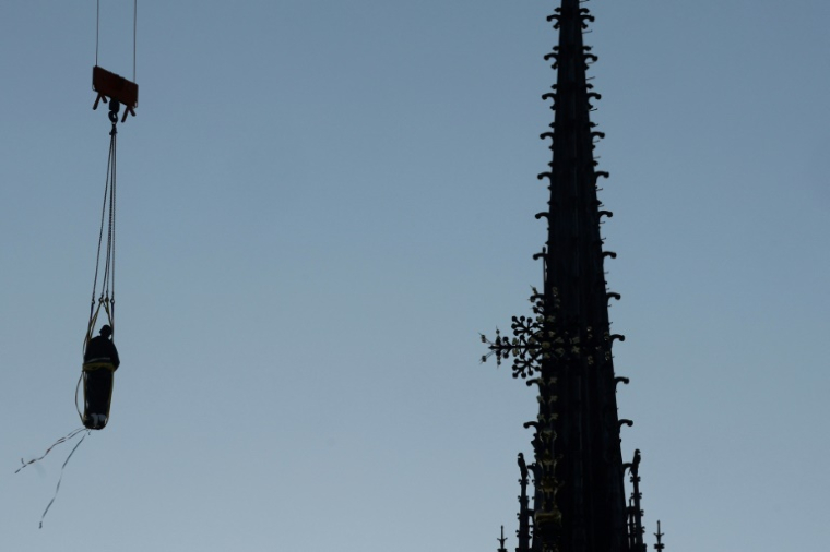 Une grue soulève l'une des 16 statues géantes d'apôtres pour la replacer sur sa base au pied de la flèche de la cathédrale Notre-Dame de Paris, le 23 juin 2025 ( AFP / GEOFFROY VAN DER HASSELT )