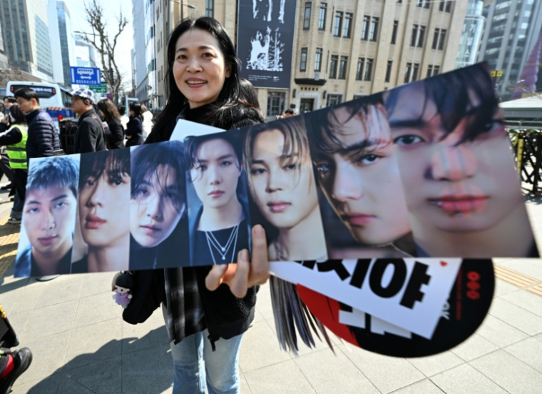 Une fan de BTS montre les photos des sept membres du groupe de K-pop, le 21 mars 2026 à Séoul ( AFP / Jung Yeon-je )