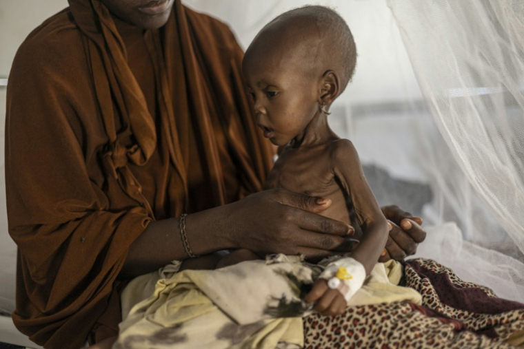 Une Somalienne récemment déplacée tient dans ses bras son bébé souffrant de malnutrition sévère dans un centre de santé, à Kismayo, le 22 avril 2026  ( AFP / SIMON MAINA )