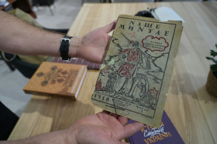 Oleksandr Savtchouk, qui joue de la bandoura, montre d'anciennes éditions ukrainiennes dans sa librairie de Kharkiv, le 18 octobre 2025 ( AFP / OLEKSII FILIPPOV )