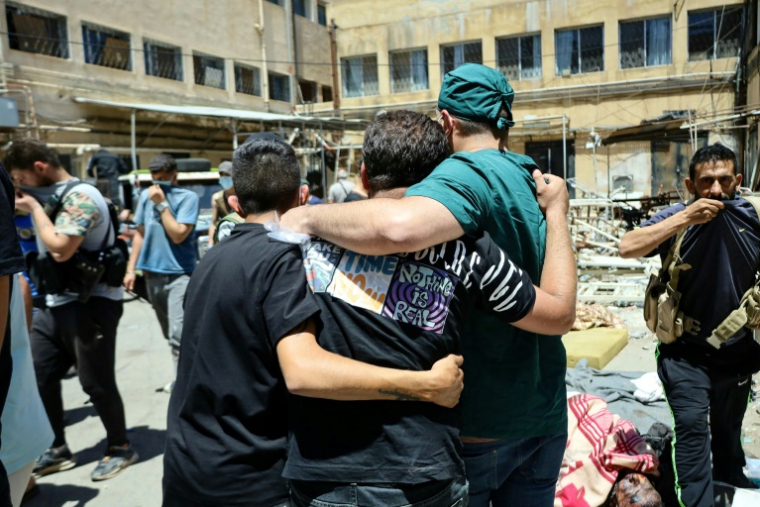 Un membre du personnel médical et d'autres hommes se tiennent parmi les corps de victimes des récents affrontements entre des combattants druzes et des tribus bédouines, disposés pour identification dans la cour d'un hôpital dans la ville de Soueida, dans le sud de la Syrie, le 17 juillet 2025 ( AFP / Shadi AL-DUBAISI )