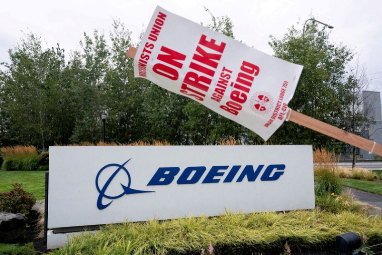 Un panneau de grève est accroché à un poteau près d'un panneau Boeing alors que des travailleurs de l'usine Boeing et des sympathisants se rassemblent sur un piquet de grève pendant le troisième jour de grève près de l'entrée d'un site de production