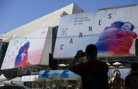 Un piéton prend une photo des affiches de la 78e édition du Festival de Cannes devant le Palais des Festivals à Cannes, dans le sud de la France, le 12 mai 2025 ( AFP / SAMEER AL-DOUMY )