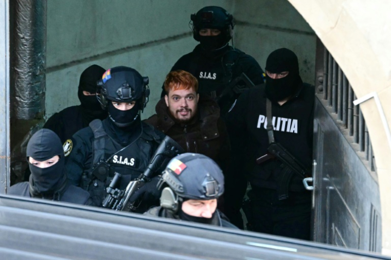 Mohamed Amra (c) escorté par des policiers, le 23 février 2025 à Bucarest, en Roumanie ( AFP / Daniel MIHAILESCU )