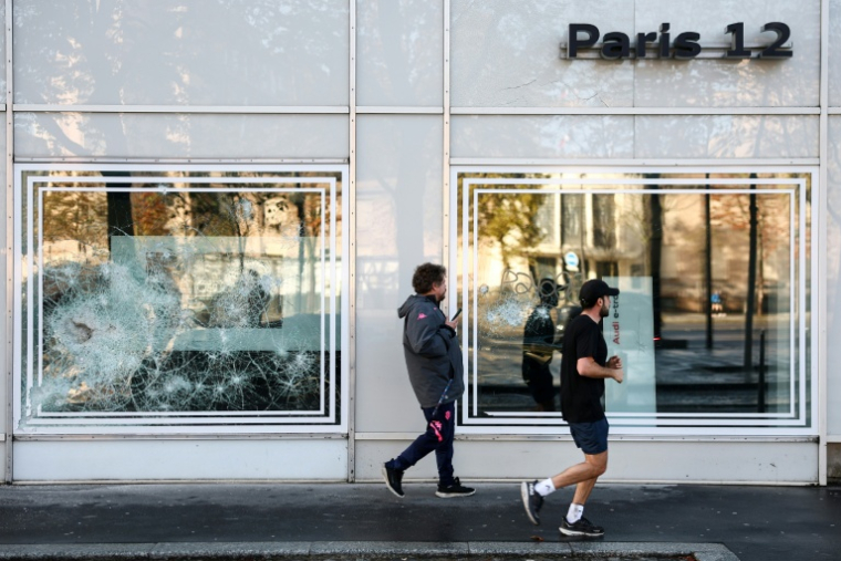 Des piétons passent devant l'enseigne d'un concessionnaire Audi dont les vitres ont été endommagées lors d'une manifestation, le 25 octobre 2026 à Paris  ( AFP / Sameer AL-DOUMY )