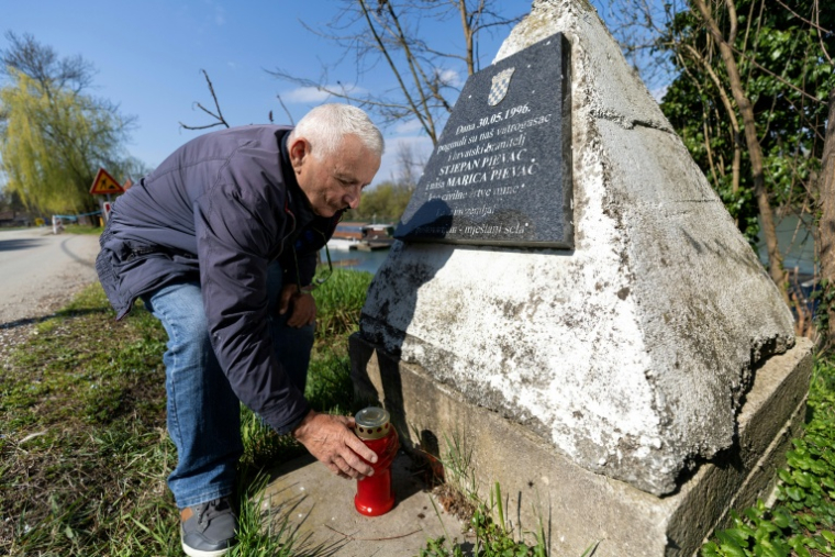 Juraj Pievac allume une bougie devant une stèle en granit, à l'endroit où il a été blessé par l'explosion d'une mine et où sa femme et son frère ont été tués,le 24 mars 2026 dans le village de Brodani, près de Karlovac ( AFP / MARKO PERKOV )
