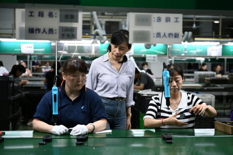 Annie Wang (c), directrice générale de l'entreprise taïwanaise Xingbao Plastic Products Co. Ltd, observe des ouvriers sur une chaîne de production à l'usine de Kunshan, dans la province orientale du Jiangsu, le 10 juin 2025 en Chine ( AFP / GREG BAKER )
