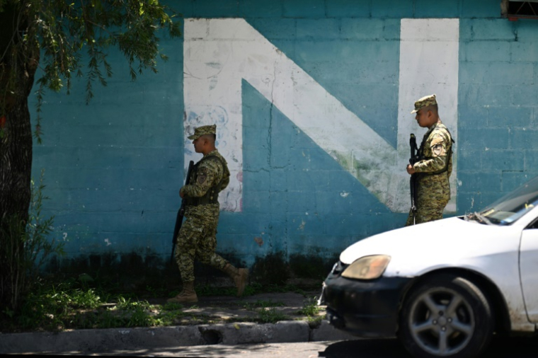 Deux soldats passent devant un graffiti faisant référence au parti Nuevas Ideas (Nouvelles idées) du président Nayib Bukele, dans le quartier du 10 de Octubre à San Marcos, au Salvador, le 14 juin 2025 ( AFP / Marvin RECINOS )