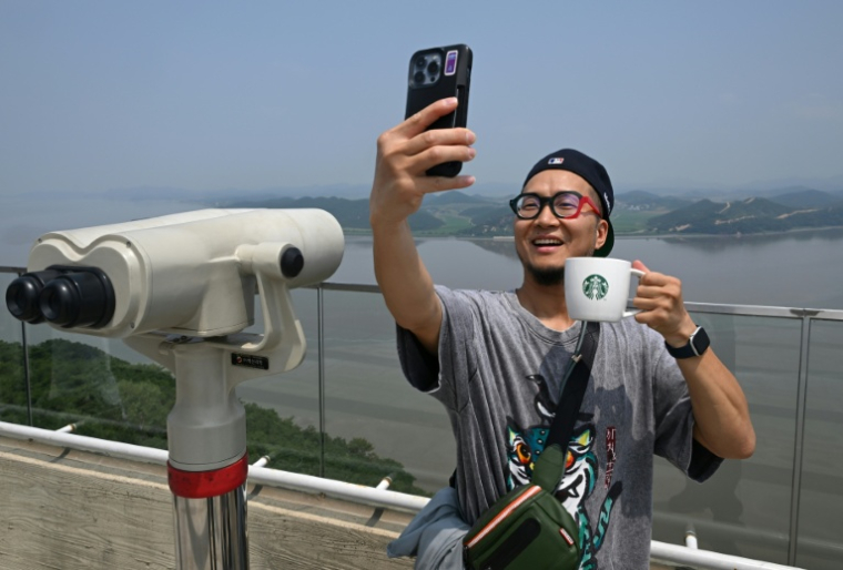 Un touriste prend un selfie avec une tasse Starbucks devant la Corée du Nord depuis une plate-forme d'observation sud-coréenne située à l'Écoparc de la Paix d'Aegibong, à Gimpo, le 1er juillet 2026  ( AFP / Jung Yeon-je )