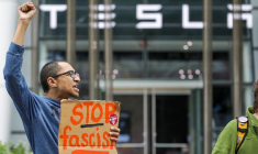 Sean Magrath lève le poing en signe de protestation lors d'une manifestation "Crappy Birthday Elon Protest" devant une salle d'exposition Tesla le jour de l'anniversaire du directeur général Elon Musk à Boston