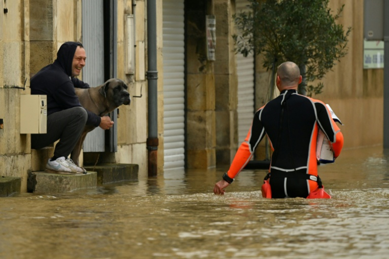 Un homme assis sur le seuil de sa maison, entourée d'eau, discute avec un pompier dans le centre-ville inondé par la Garonne, le 16 février 2026 ( AFP / Gaizka IROZ )