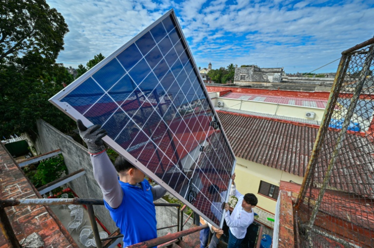 Une équipe de techniciens de systèmes photovoltaïques hisse des panneaux sur le toit d'une cantine pour personnes âgées géré par l’Eglise catholique, dans le quartier de Guanabacoa à La Havane, le 4 février 2026 ( AFP / ADALBERTO ROQUE )
