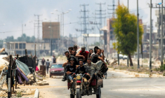 Des hommes à l'arrière d'un tricycle le long de la route de Salaheddin à Deir al-Balah, dans le centre de la bande de Gaza, le 21 juillet 2025, tandis que derrière eux s'élèvent des volutes de fumée provenant des bombardements israéliens ( AFP / Eyad BABA )