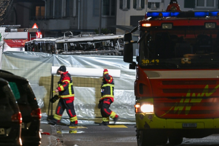 Des pompiers autour de l'autocar qui a pris feu faisant plusieurs morts, à Chiètres (Kerzers, en allemand), en Suisse, le 10 mars 2026 ( AFP / Fabrice COFFRINI )