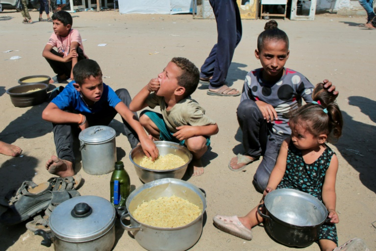 Des enfants palestiniens mangent du riz dans des casseroles après avoir obtenu des portions de nourriture auprès d'une oganisation de charité locale à Khan Younès, dans le sud de la bande de Gaza, le 27 août 2025 ( AFP / - )