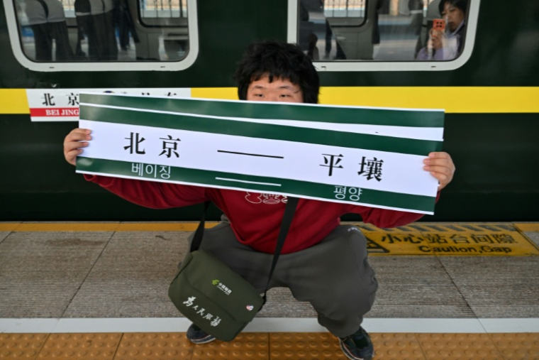 Un homme brandit une banderole "Pékin-Pyongyang" devant le train K27 à destination de Pyongyang, à la gare de Pékin, le 12 mars 2026 en Chine ( AFP / ADEK BERRY )