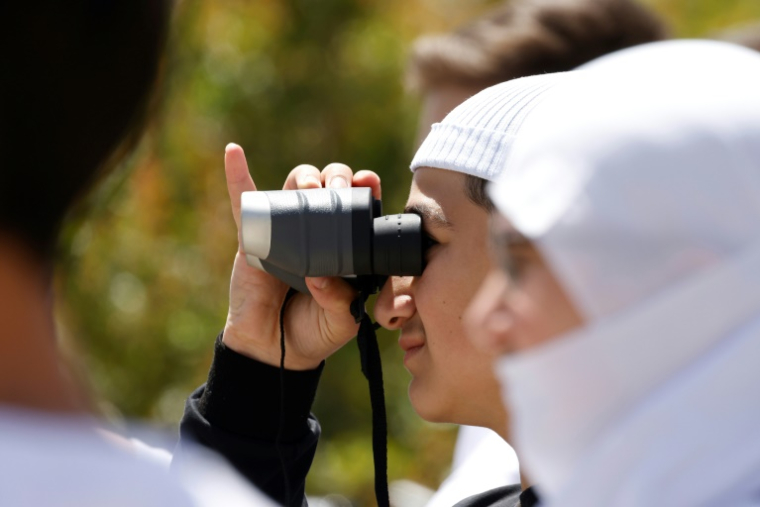 Un jeune homme druze regarde avec une paire de jumelles des proches fuyant les violences près de Damas, après leur arrivée dans la zone tampon en face du village de Majdal Shams sur les hauteurs de la partie du Golan occupée par Israël, le 3 mai 2025 ( AFP / Jalaa MAREY )