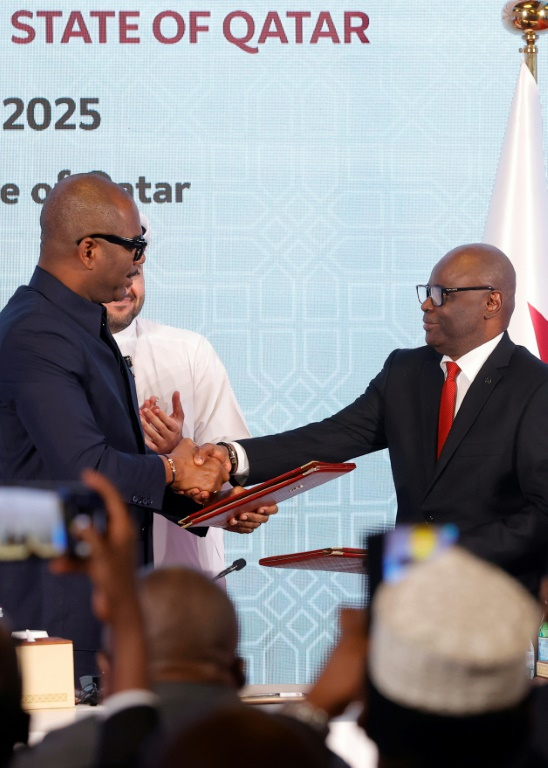 Le chef de la délégation congolaise Sumbu Sita Mambu (G) serre la main du secrétaire exécutif du groupe armé M23,  Benjamin Mbonimpa (D), après avoir signé une déclaration de principe comprenant un accord de cessez-le-feu, le 19 juillet 2025 à Doha ( AFP / Karim JAAFAR )