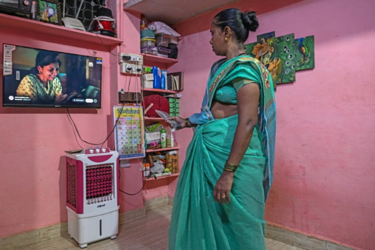 Manda Sunil Bhave, éligible à la relocalisation dans le cadre d'un projet de rénovation urbaine, regarde la télévision chez elle à Dharavi, un bidonville de Bombay, le 9 juillet 2025 en Inde ( AFP / Indranil MUKHERJEE )