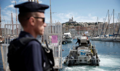 Un CRS français patrouille au Vieux-Port, avec la basilique Notre-Dame de la Garde en arrière-plan, avant l'arrivée de la flamme olympique pour les Jeux Olympiques de Paris 2024, à Marseille