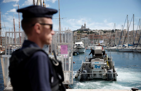 Un CRS français patrouille au Vieux-Port, avec la basilique Notre-Dame de la Garde en arrière-plan, avant l'arrivée de la flamme olympique pour les Jeux Olympiques de Paris 2024, à Marseille