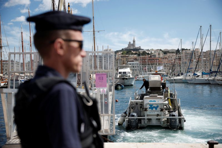 Un CRS français patrouille au Vieux-Port, avec la basilique Notre-Dame de la Garde en arrière-plan, avant l'arrivée de la flamme olympique pour les Jeux Olympiques de Paris 2024, à Marseille