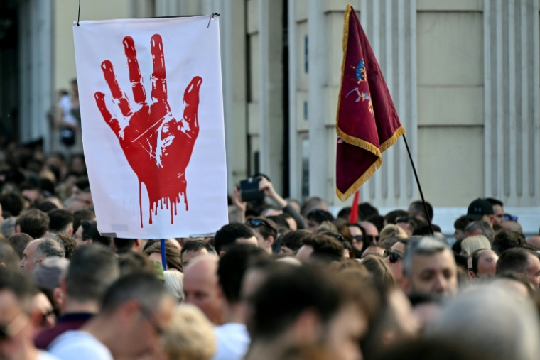Des personnes défilent derrière une banderole ornée d’une main rouge lors d’une manifestation antigouvernementale à Belgrade, le 23 mai 2026, dénonçant la corruption et réclamant des élections anticipées après l’effondrement meurtrier de l'auvent de la gare de Novi Sad, en Serbie, en 2024 ( AFP / Andrej ISAKOVIC )