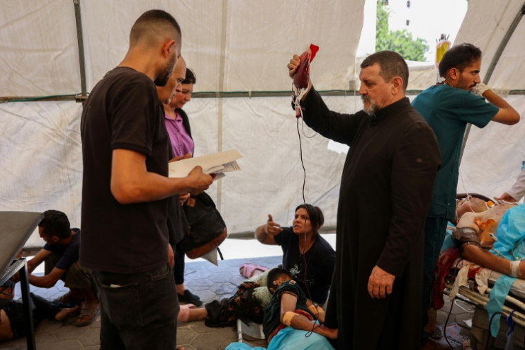 Le père Carlos (C) de l'église de la Sainte-Famille de la ville de Gaza aide à soigner les blessés à l'hôpital Al-Ahli, le 17 juillet 2025 ( AFP / Omar AL-QATTAA )