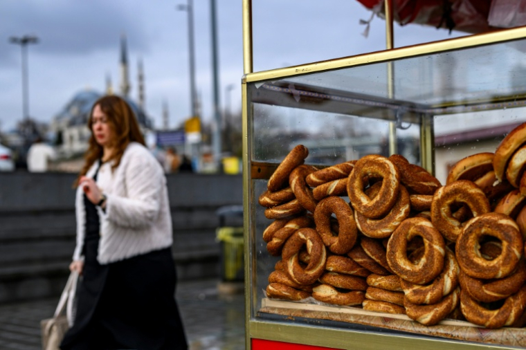 Une femme passe à côté d'un vendeur de simits, petits pains ronds turcs en forme d'anneau, le 27 décembre 2025 à Istanbul ( AFP / Yasin AKGUL )