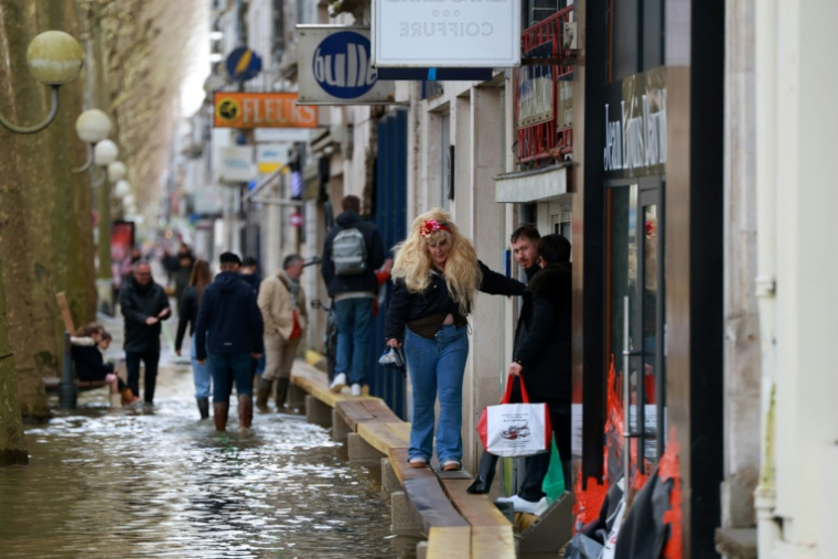 Une habitante marche sur des planches de bois dans une rue inondée par les crues, le 21 février 2026 à Saintes, en Charente-Maritime ( AFP / ROMAIN PERROCHEAU )