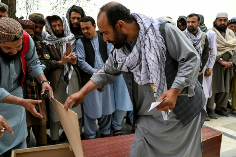 Abdul Hai Hamidi (c) regarde dans un cercueil à la recherche d'un proche lors des deuxièmes funérailles collectives des victimes tuées par une frappe aérienne pakistanaise sur un hôpital pour toxicomanes, à la mosquée Eid Gah de Kaboul le 26 mars 2026 en Afghanistan ( AFP / Wakil KOHSAR )