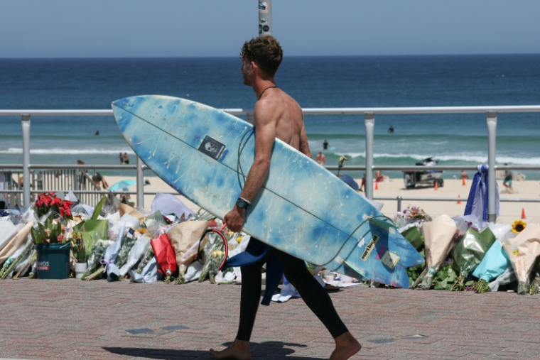 Un surfeur passe devant les fleurs déposées sur la promenade de la plage de Bondi à Sydney, le 18 décembre 2025, en hommage aux victimes de l'attentat du 14 décembre ( AFP / DAVID GRAY )