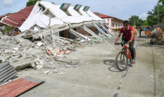 Un homme passe à vélo devant un bâtiment effondré où trois personnes ont été retrouvées mortes après un séisme à Bogo, dans la province de Cebu aux Philippines, le 2 octobre 2025 ( AFP / Ted ALJIBE )